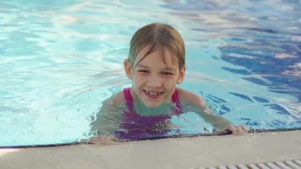 Komik küçük bir kız havuzun kenarında yardım almadan yüzmeyi öğreniyor.. — Stok video