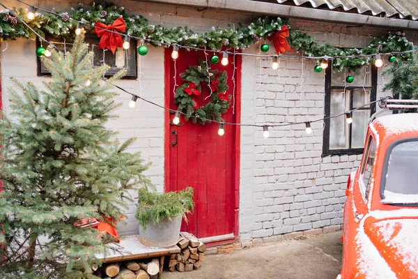 Evin verandasının yanında kırmızı kapısında yeni yıl çelengi olan kırmızı bir araba.. 