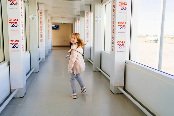 Маленькая девочка в пальто бежит и поворачивается вниз по коридору, чтобы сесть на самолет — стоковое фото
