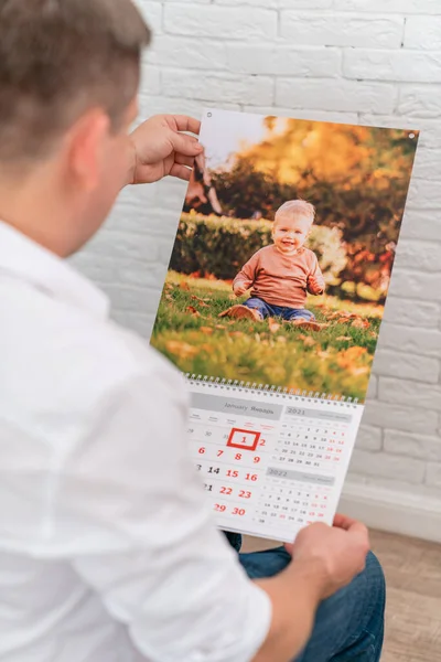 L'uomo tiene un calendario con una foto di un bambino. prodotti stampati. — Foto Stock