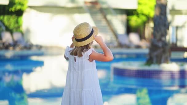 Niedliches kleines Mädchen in weißem Kleid und Strohhut am Pool in der Nähe der Villa. — Stockvideo