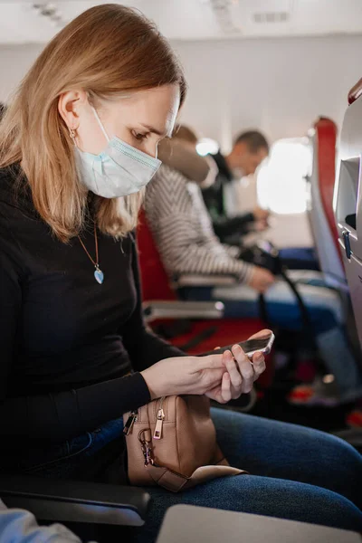 En kvinna med skyddsmask läser sms på telefonen ombord på planet. — Stockfoto
