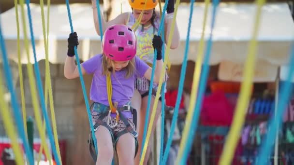 Brave little girls in a helmet, T-shirt and shorts climbs in a rope park — Stock Video