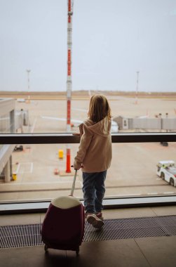 Bavullu küçük bir kız havaalanının penceresinde duruyor.. 