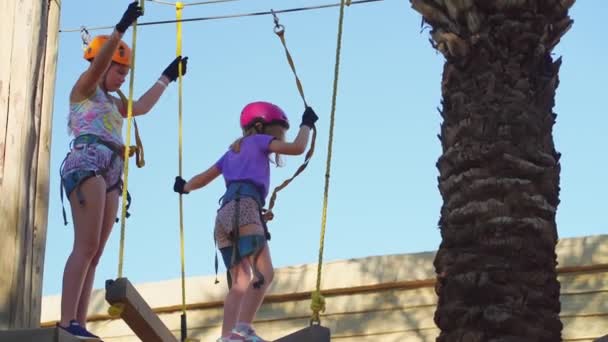Kasklı, tişörtlü ve şortlu iki cesur kız halat parkına tırmanıyor. — Stok video