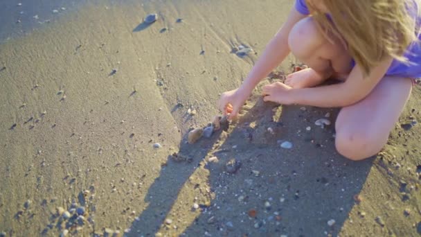 Sevimli küçük bir kız kumsalda oturuyor, kumsalda ve çakıl taşlarıyla oynuyor.. — Stok video