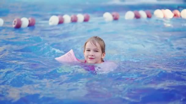 Una niña divertida nada en brazaletes inflables en una piscina — Vídeo de stock