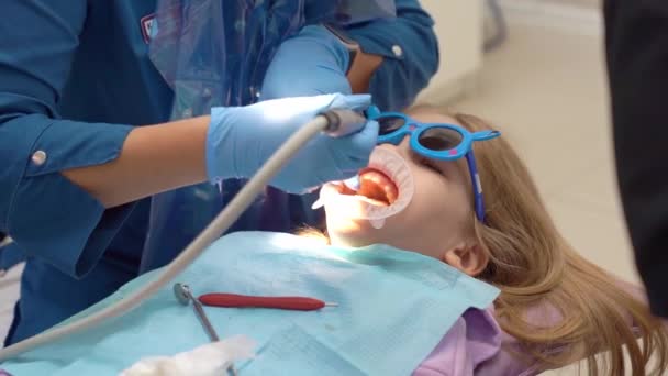 Маленькая девочка с оральным расширителем на приеме у дантиста. Полировка зубов — стоковое видео
