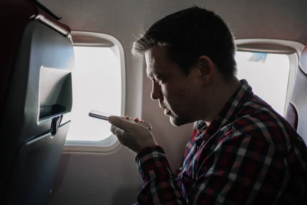 Mannen i rutig skjorta spelar in ett ljudmeddelande på telefon i sittplats ombord på planet. — Stockfoto