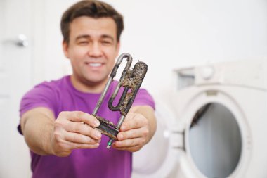 Çamaşır makinesinin tamircisi eski boru elektrikli ısıtıcıyı tutuyor. 