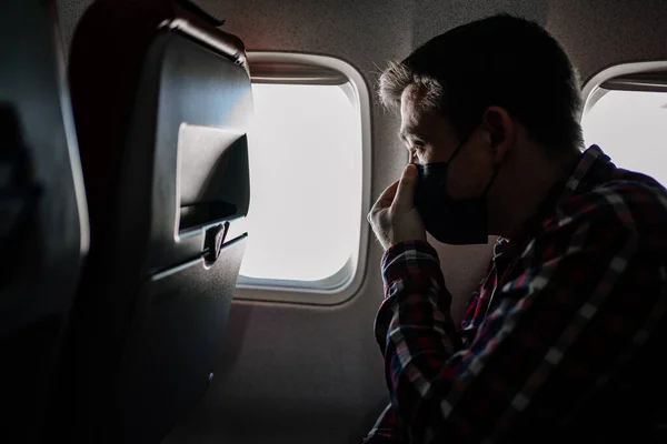Человек исправляет черную защитную маску и клетчатую рубашку у окна самолета. — стоковое фото