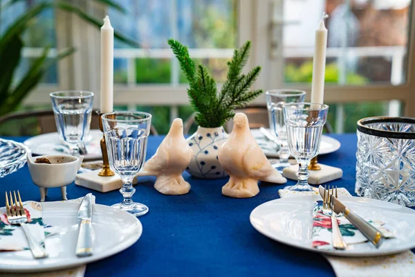 Asztal kék terítővel, galambokkal, lucfenyő ágakkal és asztali árukkal. — Stock Fotó