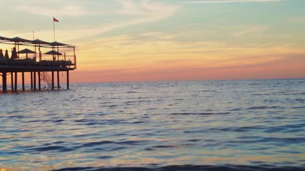 Piękny zachód słońca nad morzem. molo z parasolami i leżakami dla wczasowiczów — Wideo stockowe