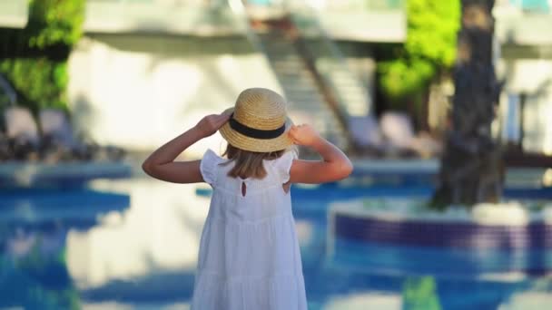 Мила маленька дівчинка в білій сукні і солом'яний капелюх біля басейну біля вілли . — стокове відео