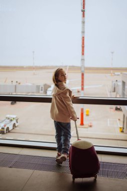 Bavullu küçük bir kız havaalanının penceresinde duruyor.. 