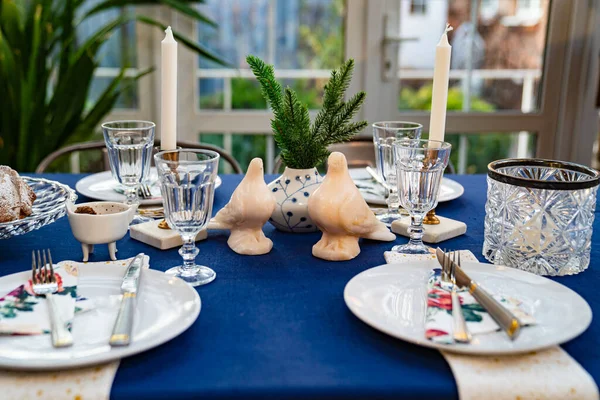 Stůl s modrým ubrusem, holuby, smrkovými větvemi a stolním nádobím. — Stock fotografie