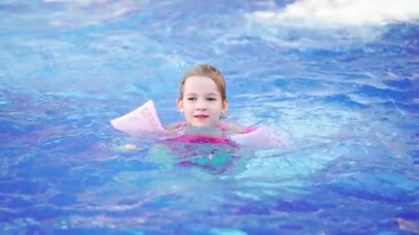 Una niña divertida nada en brazaletes inflables en una piscina — Vídeos de Stock