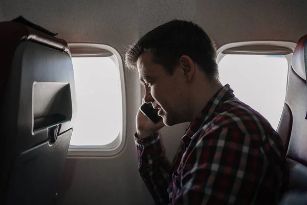 Man i rutig skjorta samtal på telefon i sätet för passagerare ombord på planet. — Stockfoto