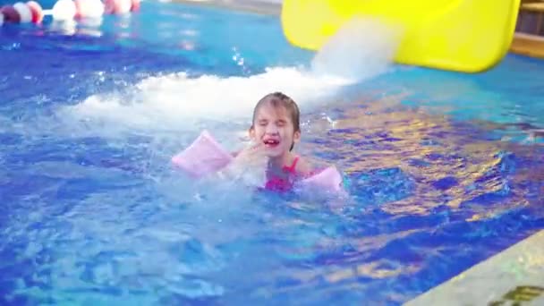 Ένα αστείο κοριτσάκι κολυμπάει σε φουσκωτά περιβραχιόνια σε μια πισίνα. — Αρχείο Βίντεο