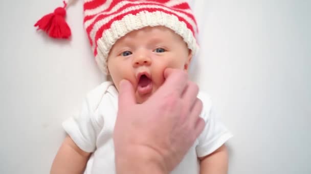 Tangan menyentuh wajah lucu anak kecil di topi dari peri Natal atau gnome.baby santa — Stok Video