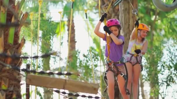 Moedig meisje in helm, paars T-shirt en korte broek bang en klimt in een touw park — Stockvideo