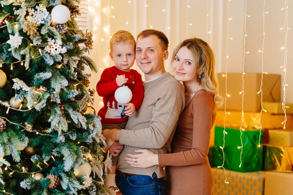 Genç bir oğlu olan güzel ve mutlu bir aile Noel ağacını süslüyor.