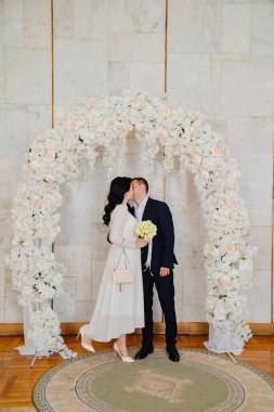 Nüfus dairesinde gelin ve damat bir çiçek kemerinde öpüşürler..