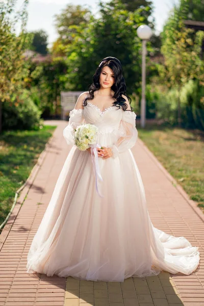 Brünette Braut im Kleid mit einem Blumenstrauß auf dem Weg in den Park. — Stockfoto