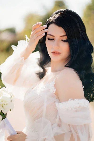 Brünette Braut in einem Kleid mit einem Blumenstrauß im Freien — Stockfoto