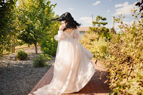 Blick von hinten. eine Braut, die im Hochzeitskleid einen Weg im Park hinunterläuft. — Stockfoto