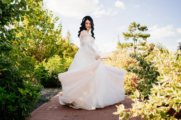 Eine schöne Braut im Brautkleid wirbelt und tanzt auf dem Weg im Park. — Stockfoto