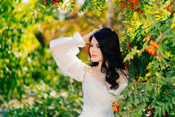 Attraktive brünette Braut im Brautkleid in einem Park mit Ebereschen. — Stockfoto