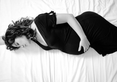 Yatakta siyah elbiseli çekici hamile bir kadın.