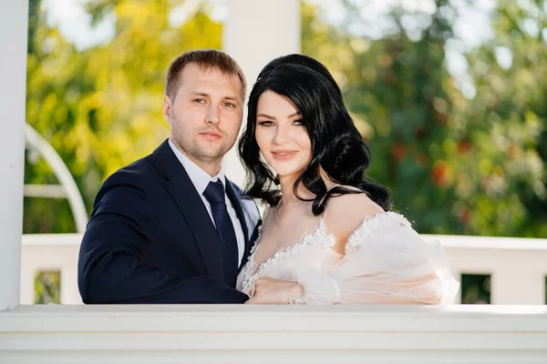 Bride and groom in wedding clothes at railing in gazebos or rotunda in the park. — Stockfoto
