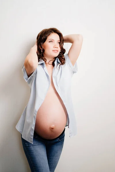 Attractive pregnant woman in jeans and a shirt on a naked body. womens health — Stockfoto