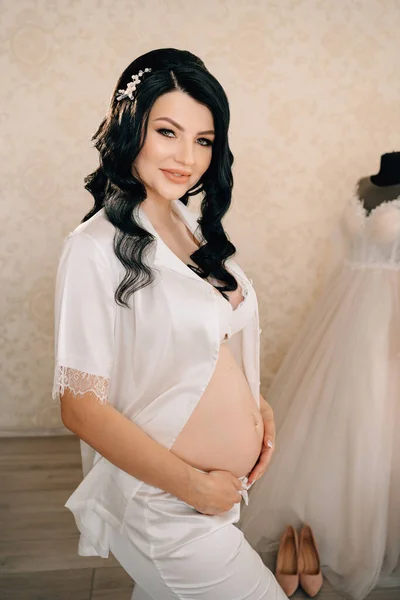 하얀 잠옷을 입고 배만 벙벙거리는 아름다운 임신 한 신부 갈색 머리. — 스톡 사진