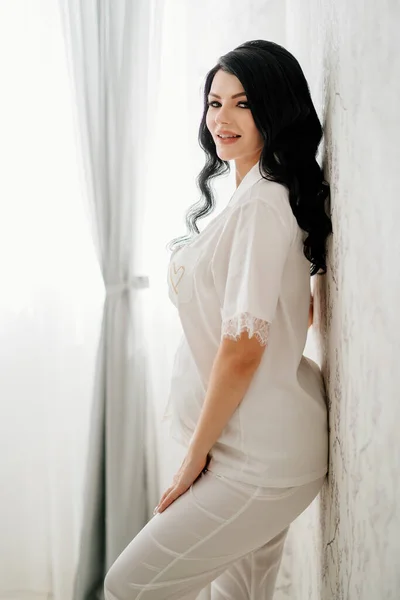 Beautiful pregnant bride brunette in white pajamas. — Stockfoto