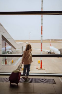 Bavullu küçük bir kız havaalanının penceresinde duruyor.. 