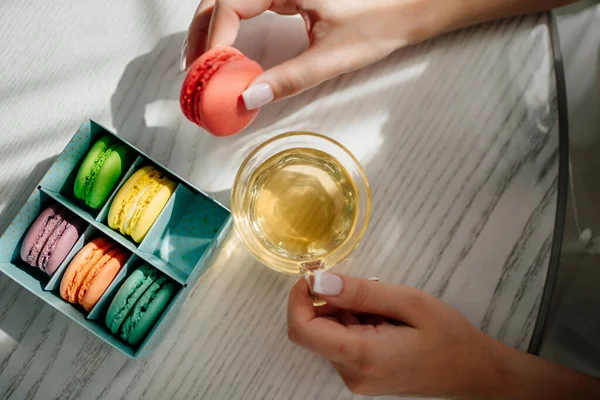 Womens hands with manicure with a cup of green tea and colorful macaroons cakes — Stock Photo, Image
