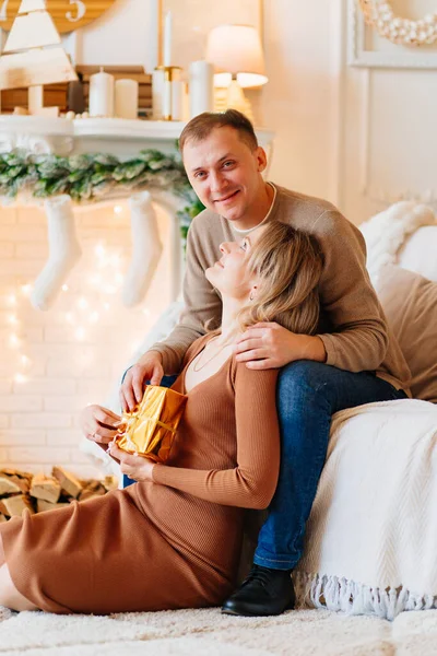 Ένα ζευγάρι ερωτευμένο με ένα δώρο σε ένα κουτί δίπλα στο χριστουγεννιάτικο τζάκι. — Φωτογραφία Αρχείου