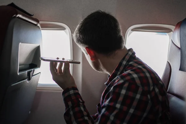 Hombre de camisa a cuadros escuchando un mensaje de audio en el teléfono en el asiento a bordo del avión — Foto de Stock