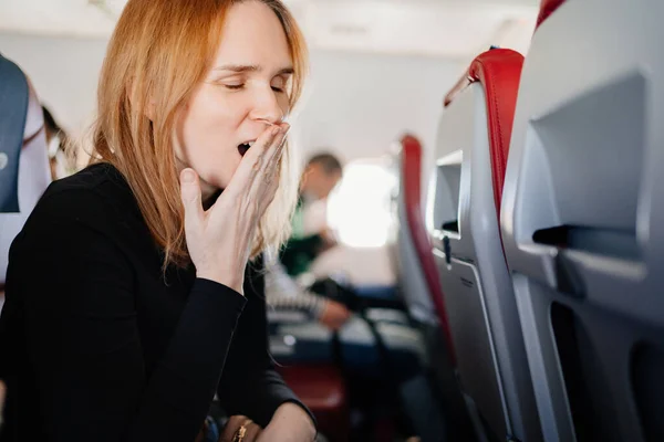 En sömnig kvinna gäspar i en flygplansplats. långa flygningar. — Stockfoto