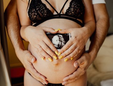 Bir erkeğin ve bir kadının elleri, çocuklarının ultrasonunu karnında taşır.