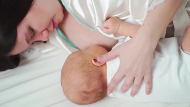 Amamentação. mãe em um robe alimenta o bebê com leite materno deitado na cama — Vídeo de Stock