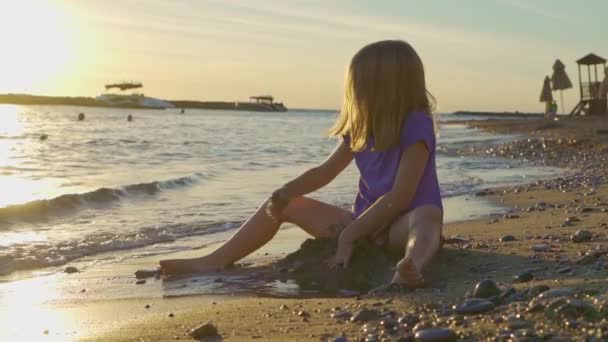 Klein meisje aan zee, verzamelt stenen en gooit ze in het water. — Stockvideo