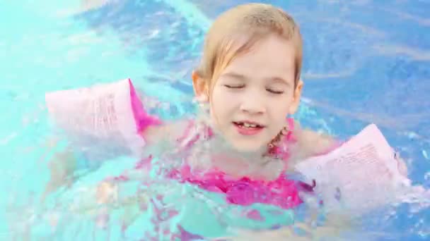 Смішна дівчинка плаває і грає в надувних пов'язках у басейні — стокове відео