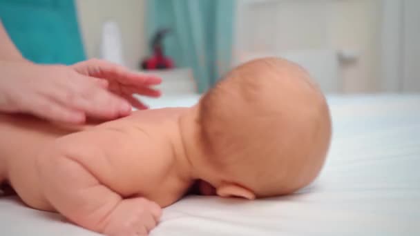 El bebé se acuesta boca abajo sobre una sábana blanca. y las manos de las mamás masajean la espalda. — Vídeo de stock