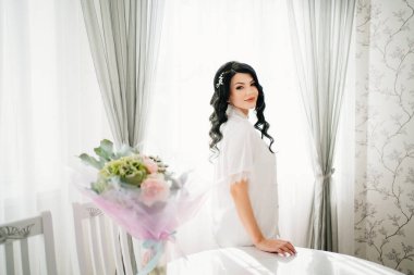 Beyaz pijamalı hamile gelin, pencere kenarındaki masa ve buketli.. 