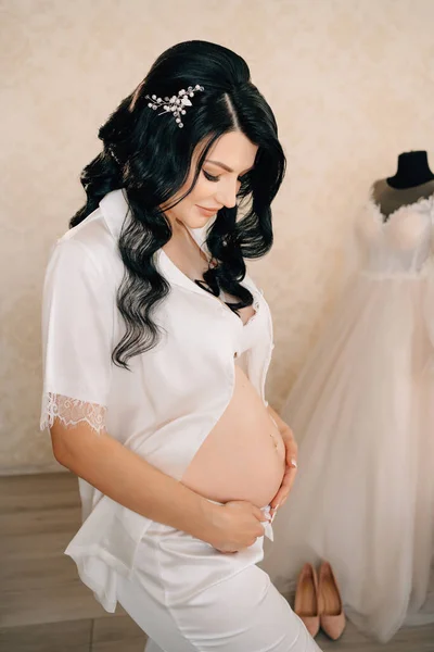 하얀 잠옷을 입고 배만 벙벙거리는 아름다운 임신 한 신부 갈색 머리. — 스톡 사진