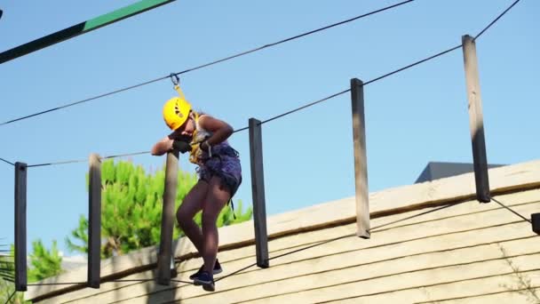 Een tiener meisje in een helm, T-shirt en korte broek klimt in een touw park — Stockvideo